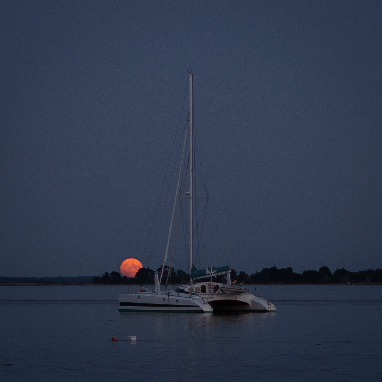 Voilier au mouillage devant la lune à l’horizon