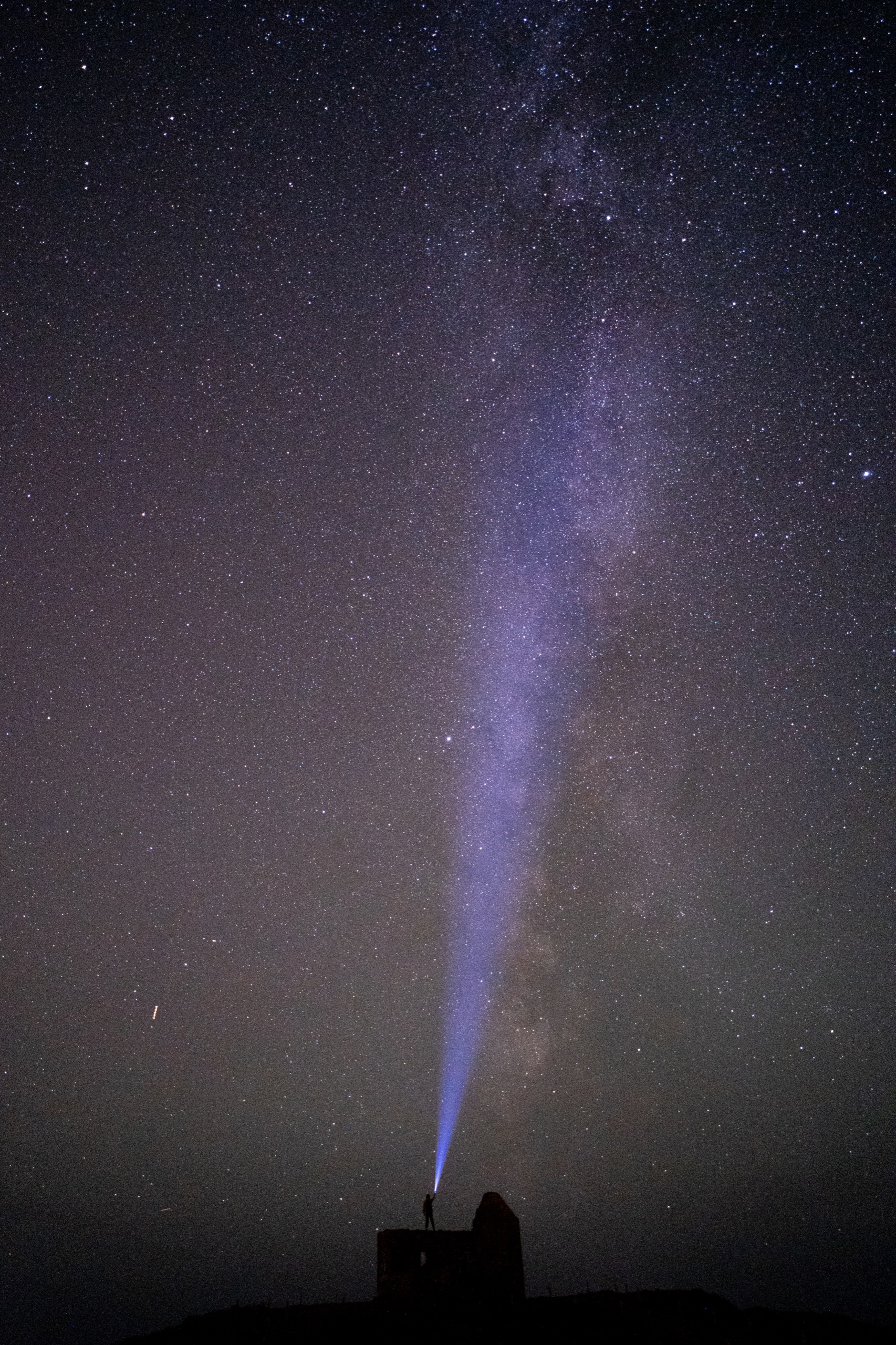 Silhouette projetant un faisceau lumineux sous la Voie lactée