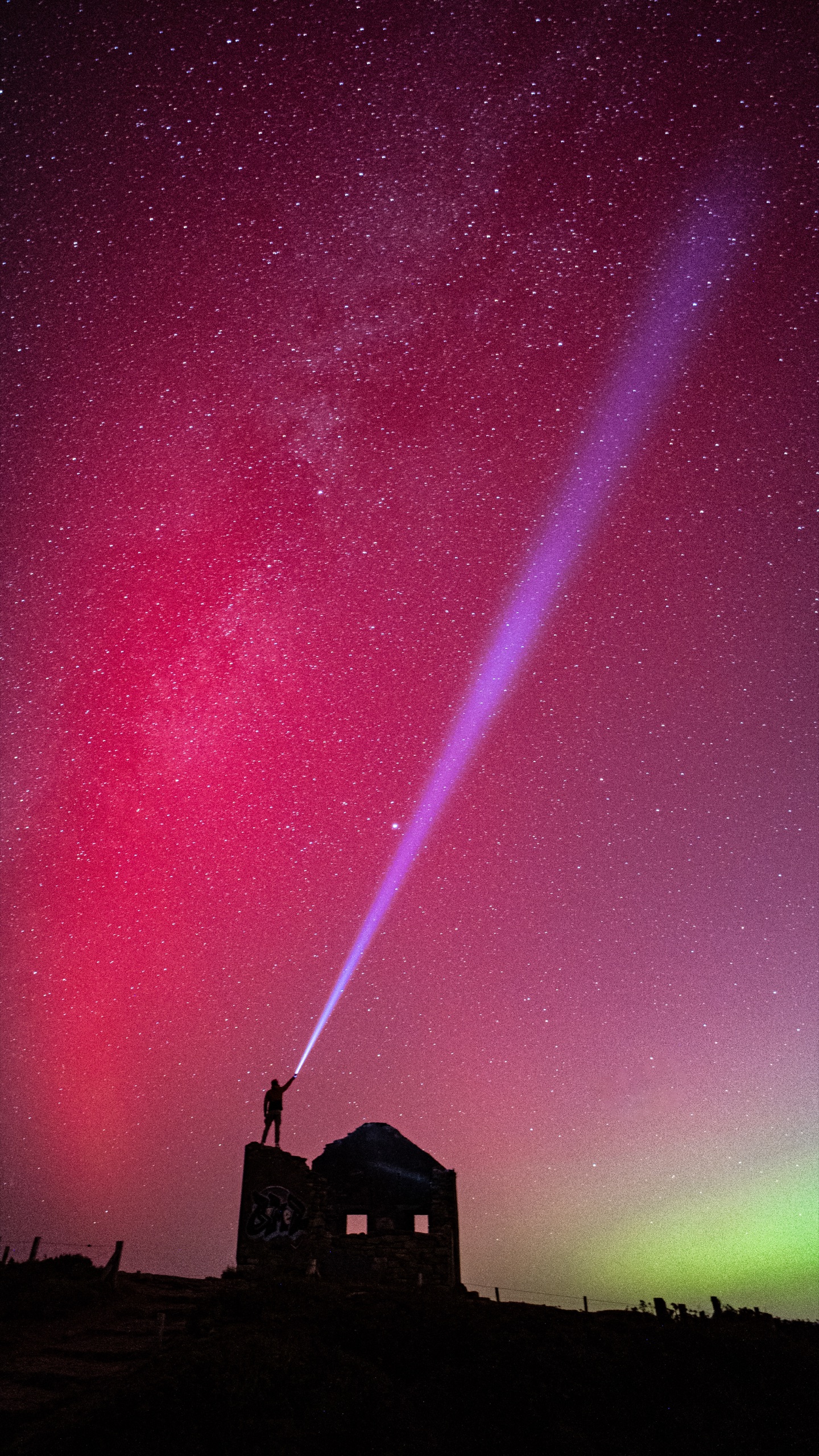 Silhouette sous une aurore boréale rouge projetant un faisceau vers les étoiles