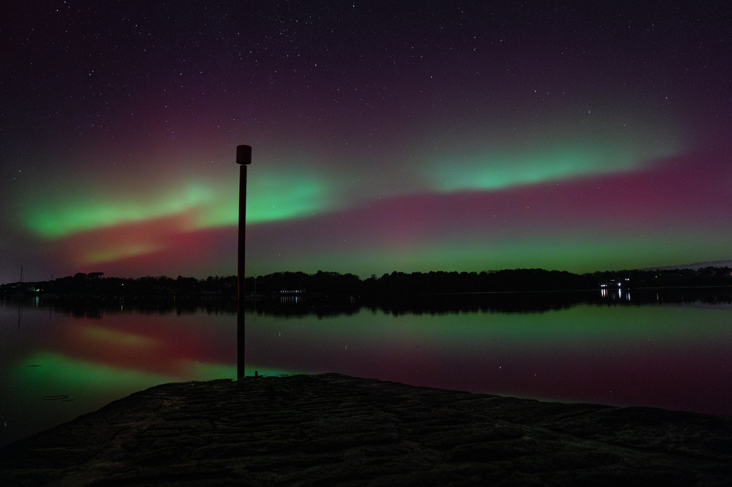 Aurore boréale verte et rouge se reflétant sur un lac
